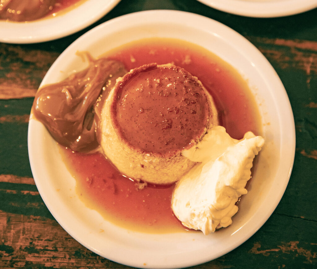 Flan with dulce de leche, whipped cream and caramel sauce served on a white plate.