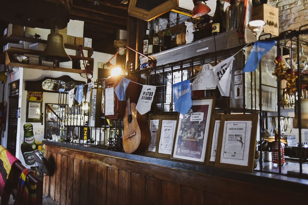 A guitar, framed pictures and old bottles on top of a wooden counter.