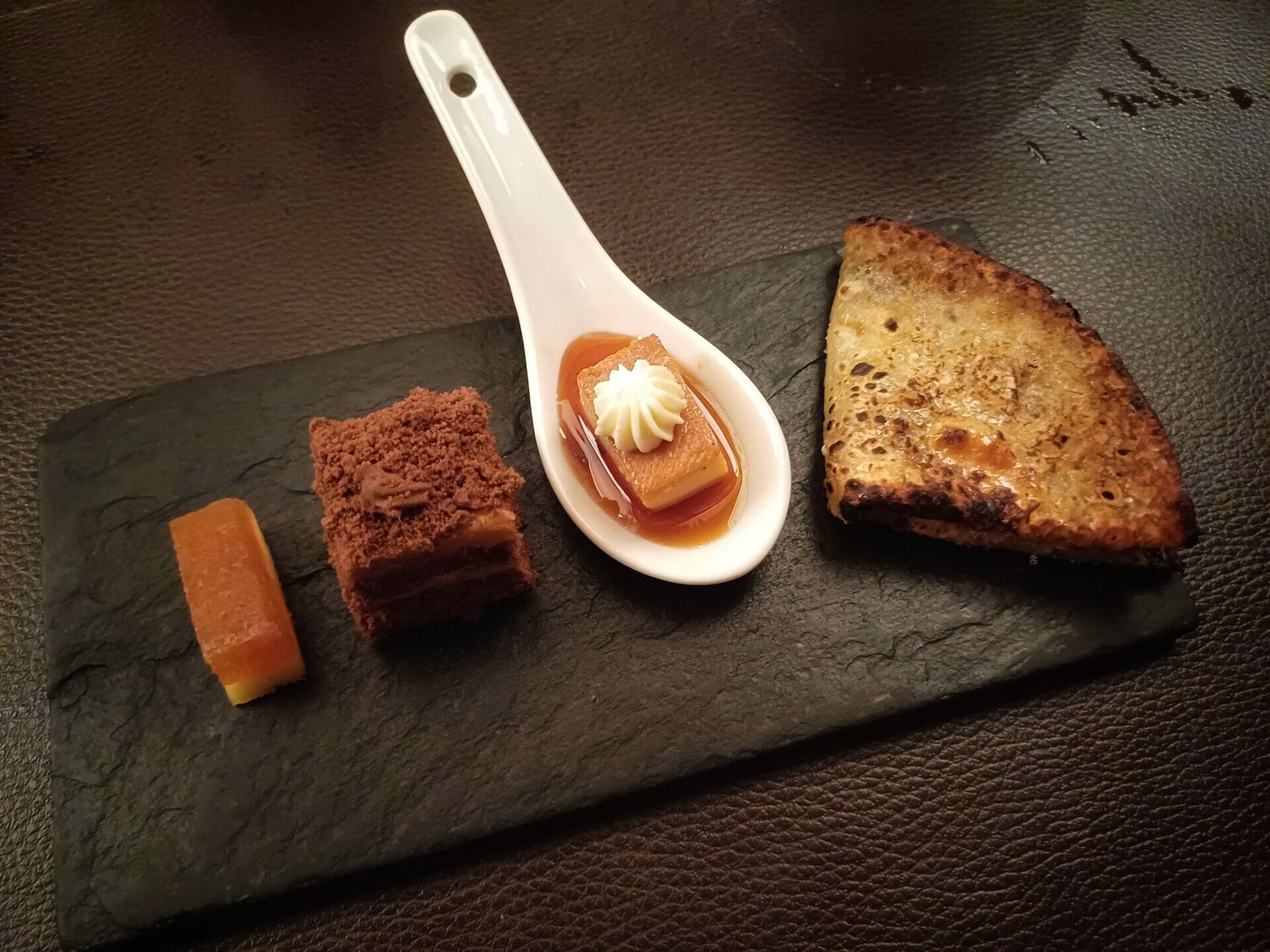 A selection of argentinian desserts on a black tray, from left to right: queso y dulce, chocotorta, flan and panqueque with dulce de leche,