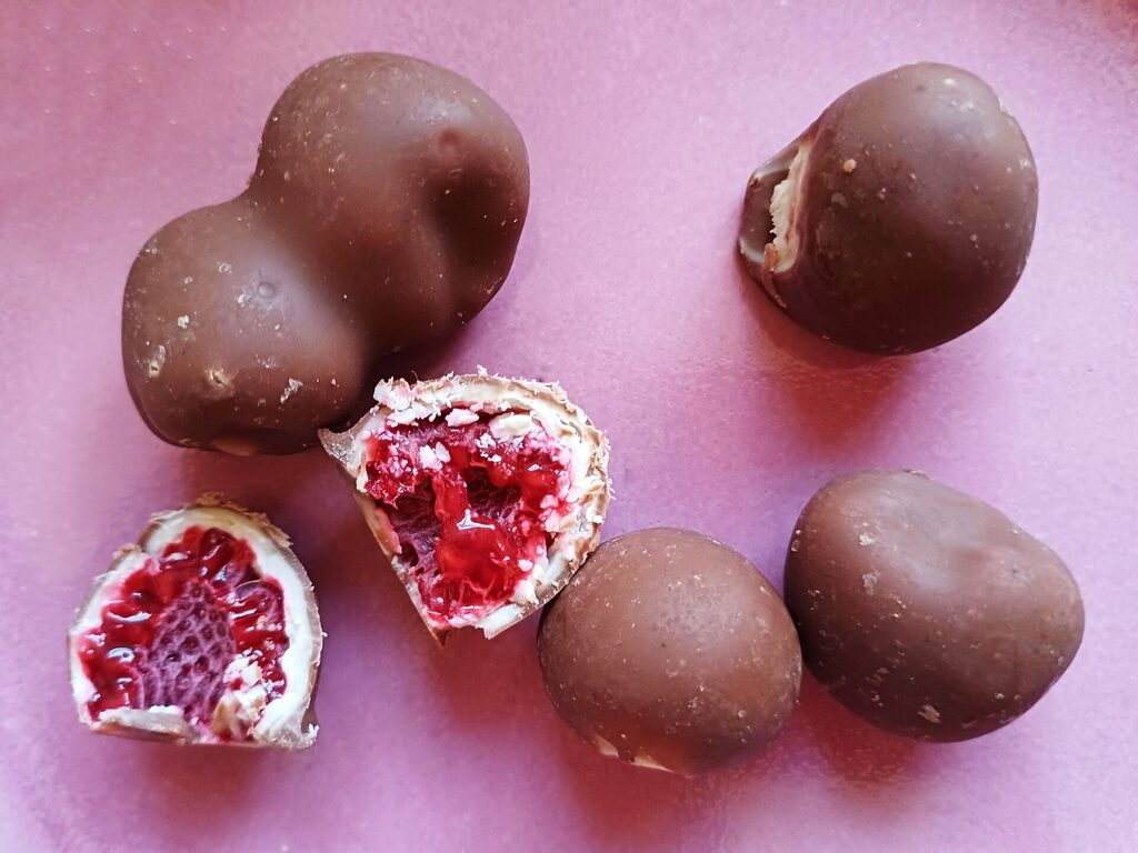 Chocolate coated frozen raspberries, known as "Franui", scattered around a pink porcelain plate.