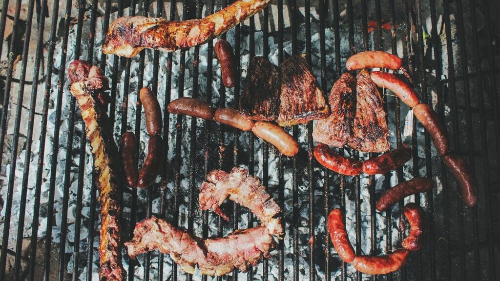 Tira de asado (spare ribs), chorizos (sausage) and vacío (flank steak) cooking on a parrilla (Argentine grill).
