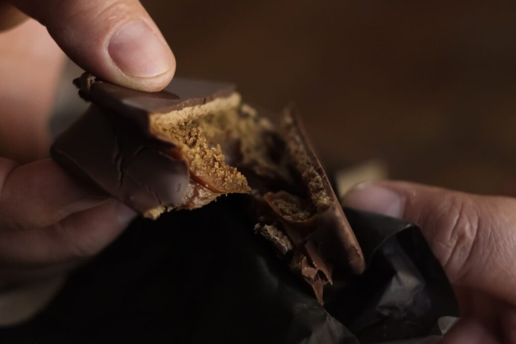 Dark chocolate alfajor with dulce de leche filling split being split into two halves.