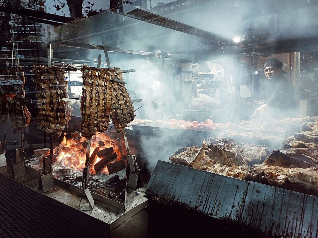 Several meats are cooked on a giant parrilla (grill).