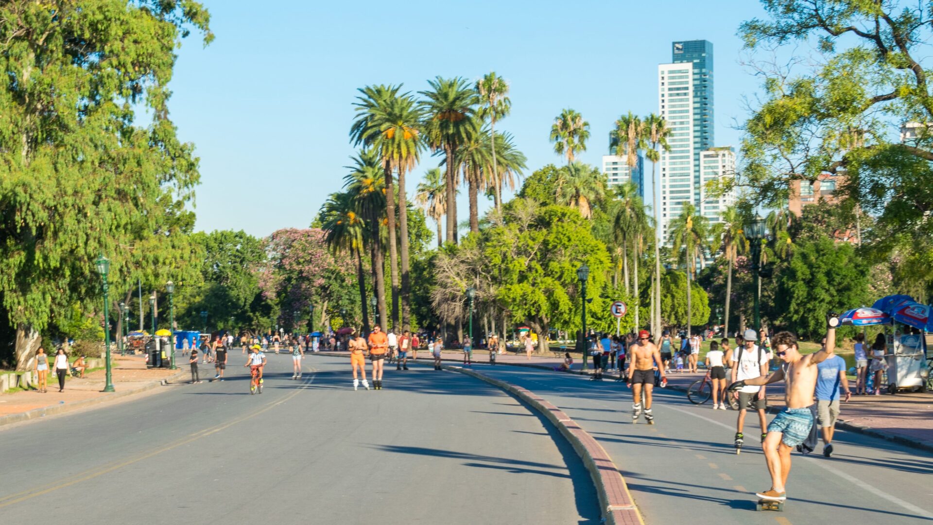 Part of the track that circles the Rosedal Rose Garden in Palermo, Buenos Aires. There are palm trees in the background and people wearing summer clothes are running or walking around.
