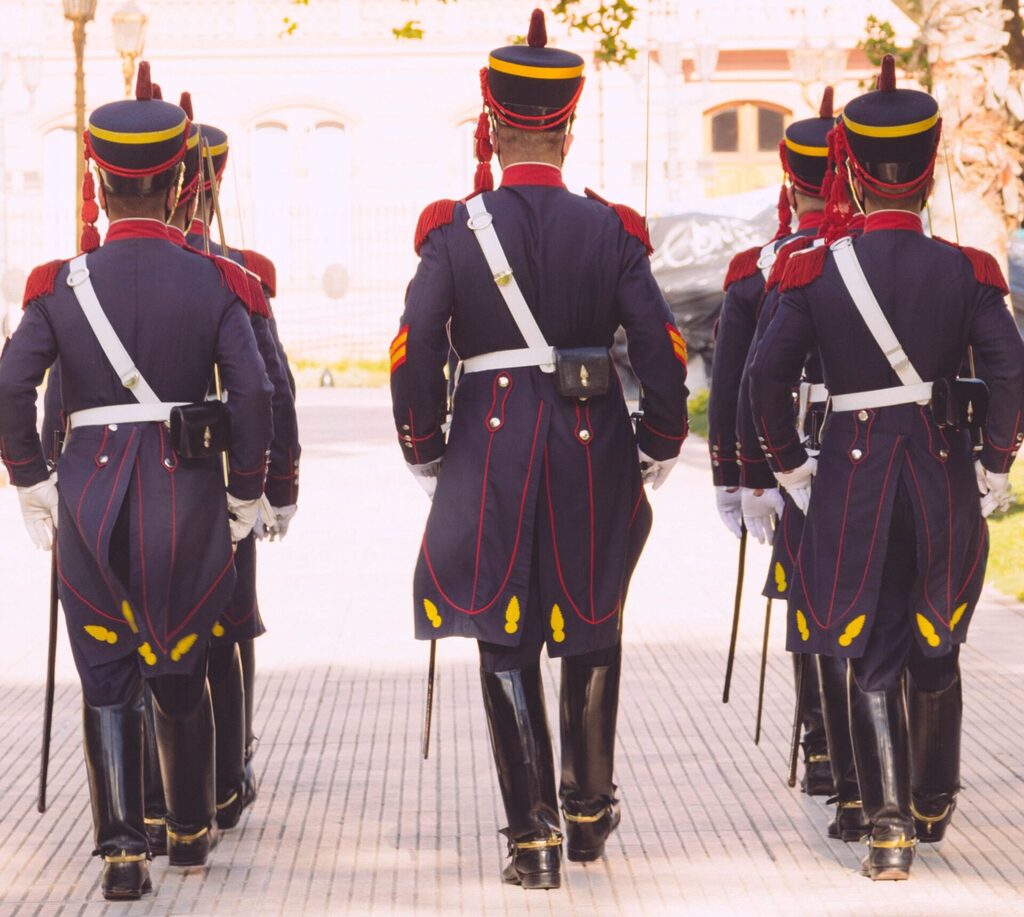 The Argentien Honor Guard, the Granaderos, marching along an unknown Buenos Aires street. The photo is taken from behind. The guards are wearing the standard blue uniform.