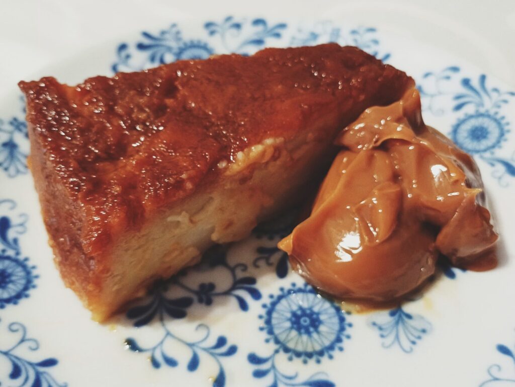 Budín de pan with a dollop of dulce de leche served on a white porcelain plate with blue motifs.