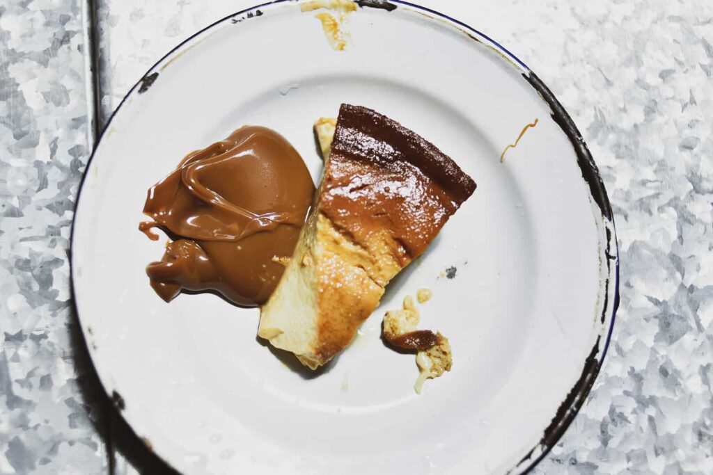 A slice of flan with dulce de leche on a white plate.