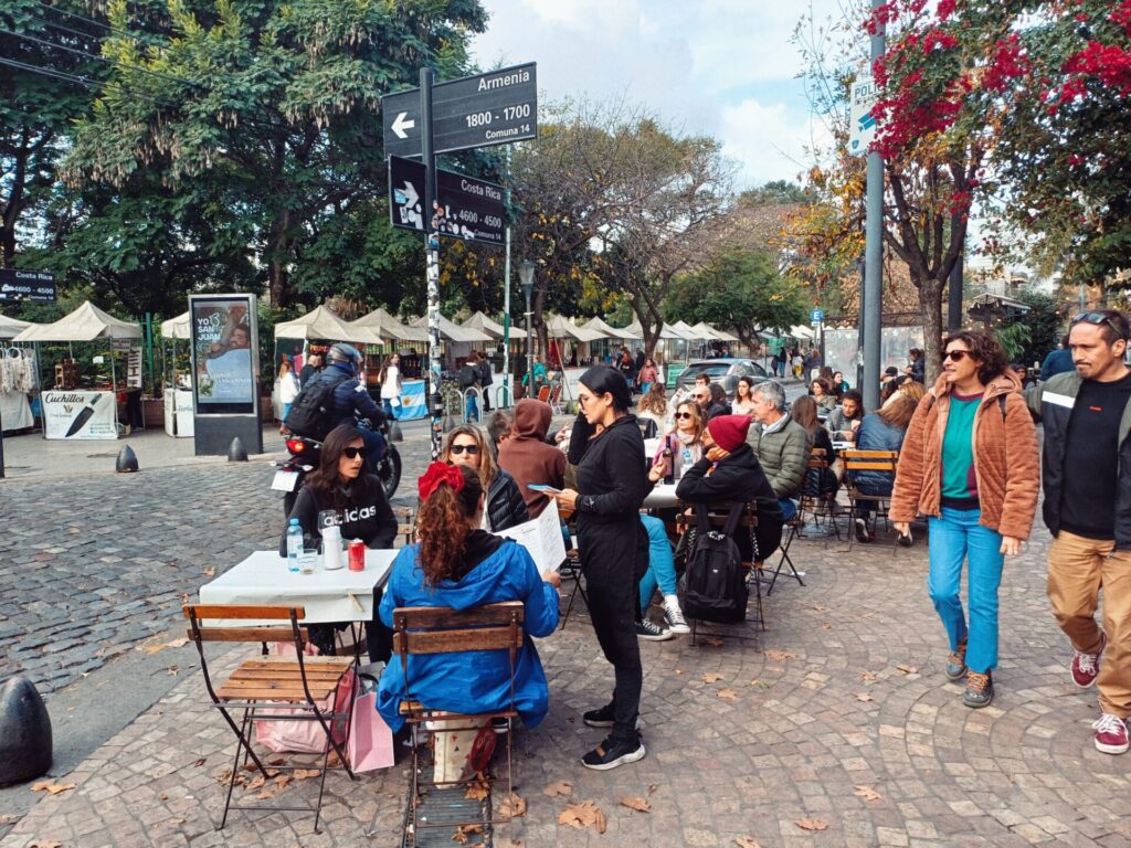 People ordering food at a restaurant in Palermo Soho. The street market on Plaza Armenia is on the background.