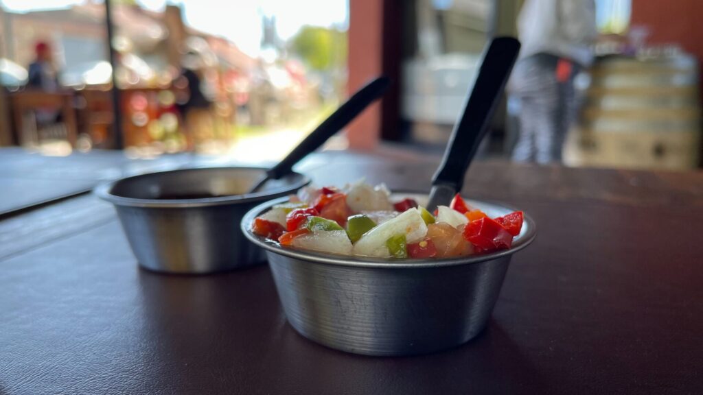 Salsa criolla (uncooked sauce made with chopped onion, red pepper,, tomato and garlic) served on a small metal container and with a small spoon.